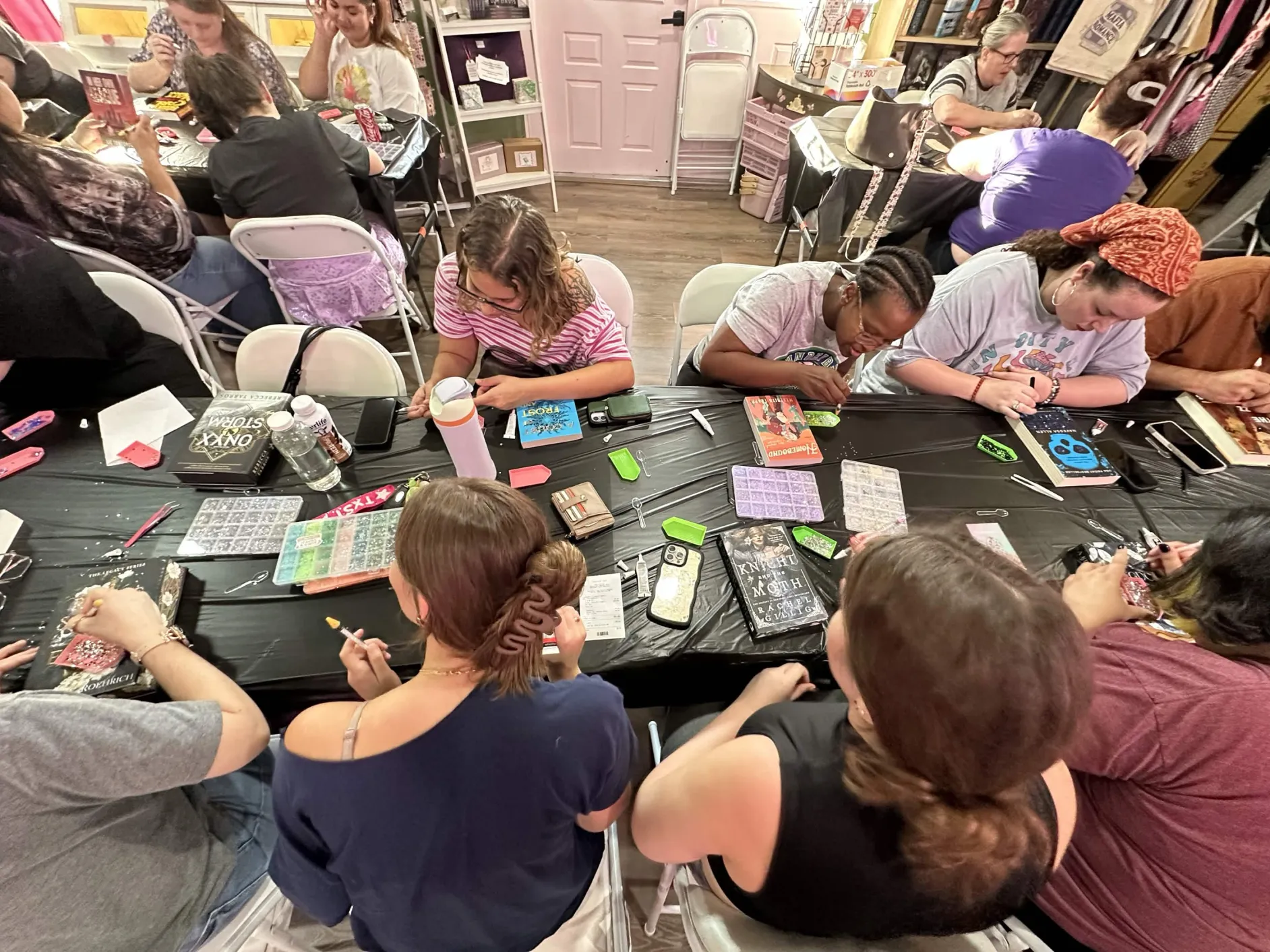 Group of children and adults sitting at tables working on crafts or activities in a classroom or workshop setting.