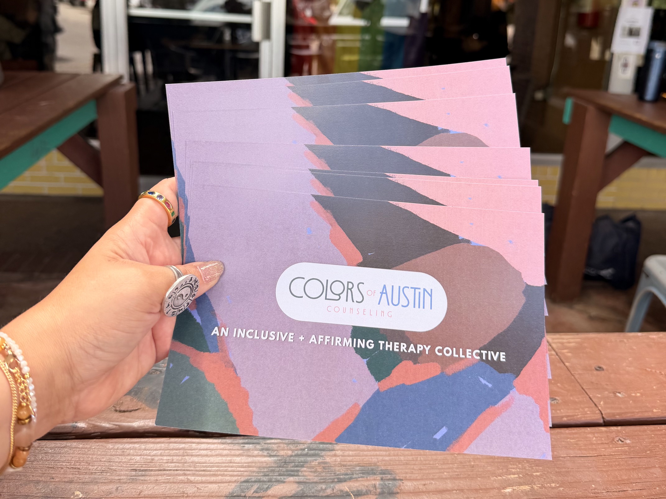 Hand holding colorful booklet with abstract design and text, background shows a store interior.