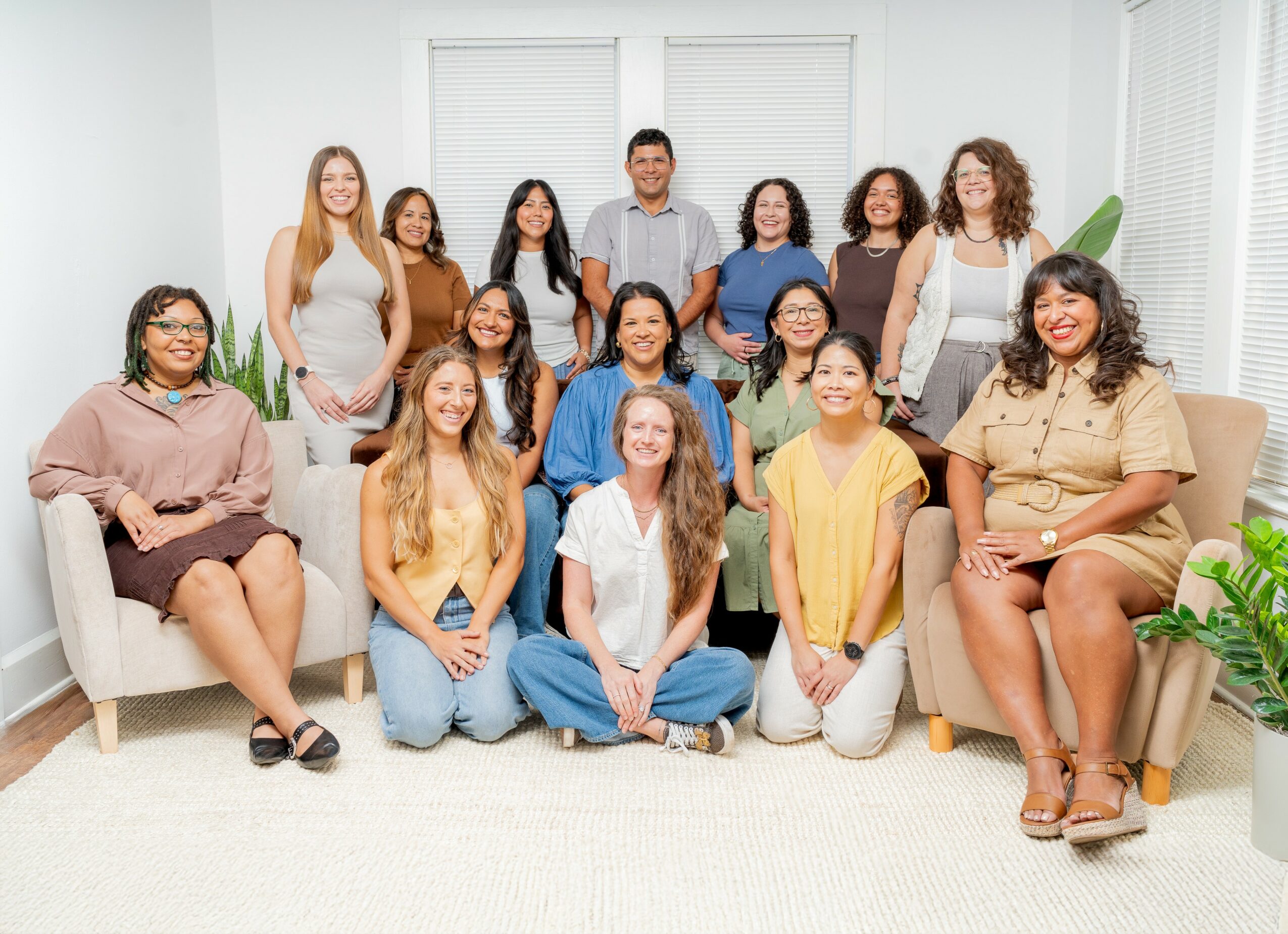 Group of 15 diverse people gathered in a bright living room, some sitting on sofas and others standing behind.
