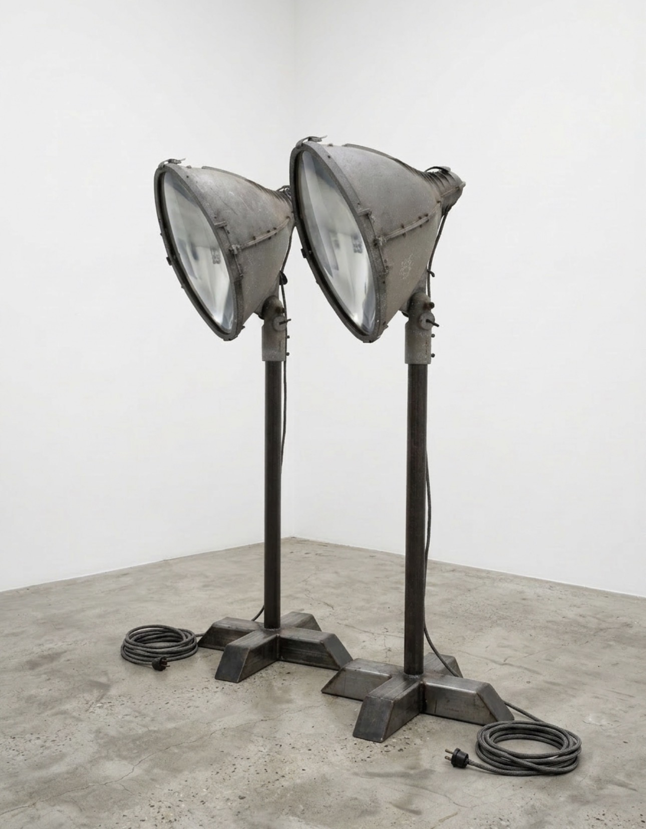 Two large, industrial-style studio lights on stands in a minimal room with a concrete floor and white walls.