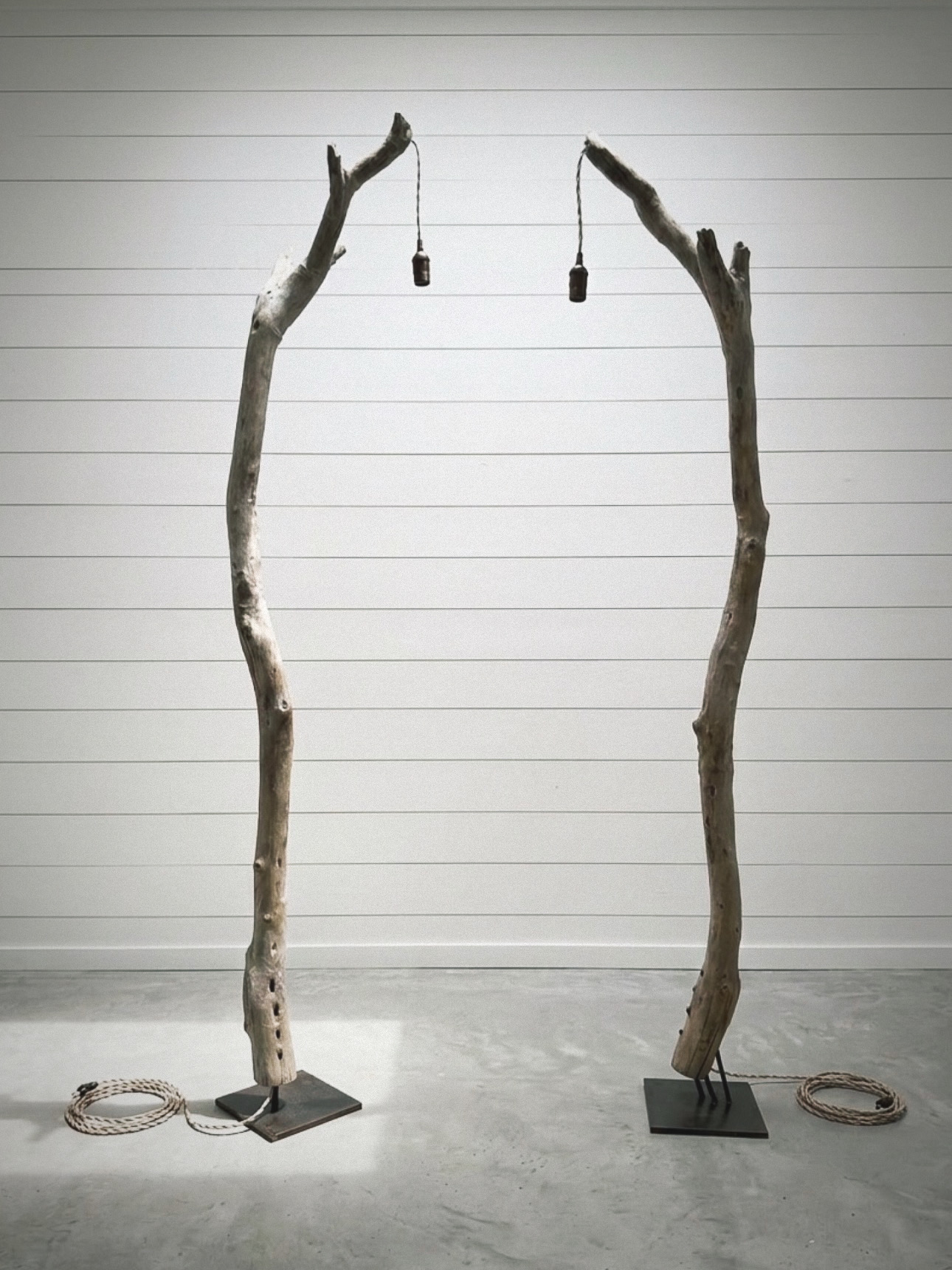 Two tall, curved wooden poles with light bulbs hanging between them, set against a white wall with horizontal lines.