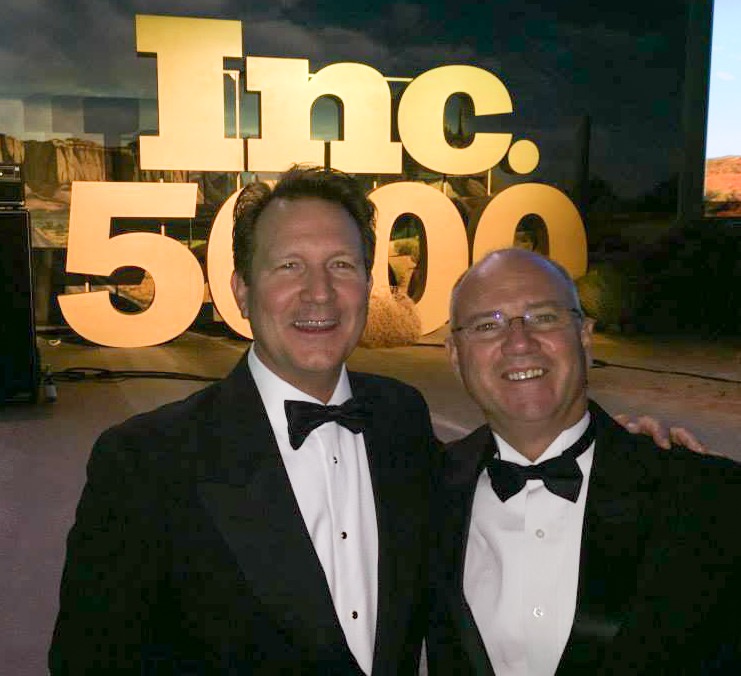Two men in tuxedos smiling at an event with a large 'Inc. 5000' sign behind them.
