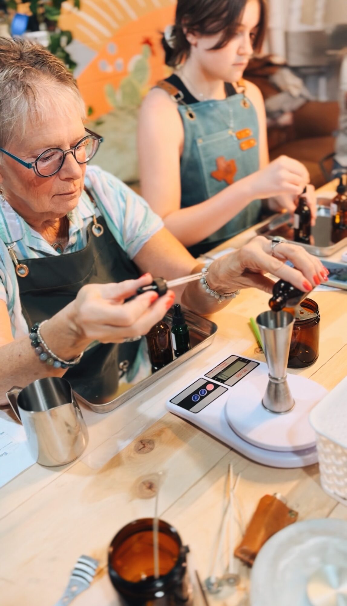 Two women working with nail polish at a table, one older and one younger, with various tools and bottles present.