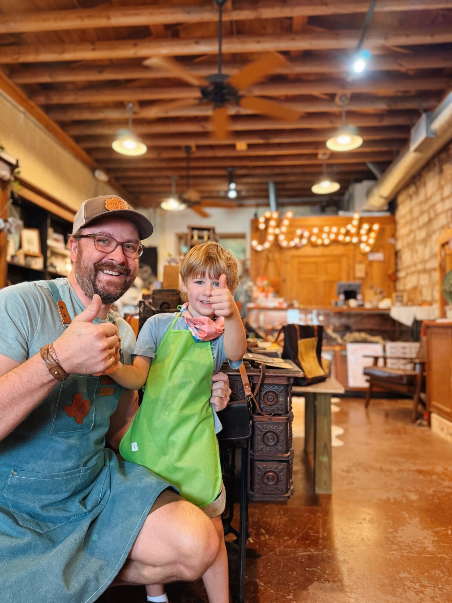 Man and child smiling inside a cozy cafe with wooden ceiling and brick walls.