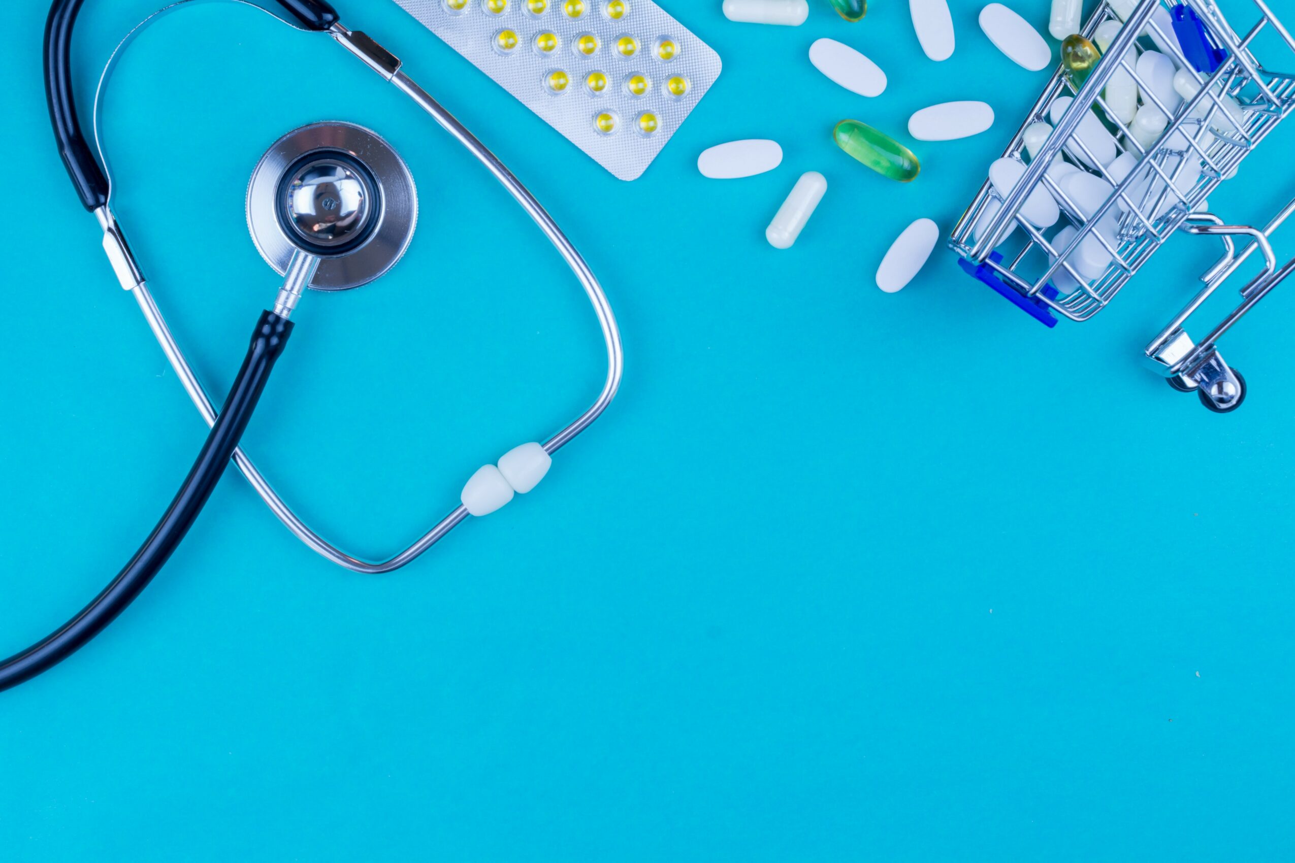 Stethoscope, pills, and a small shopping cart on a blue background.