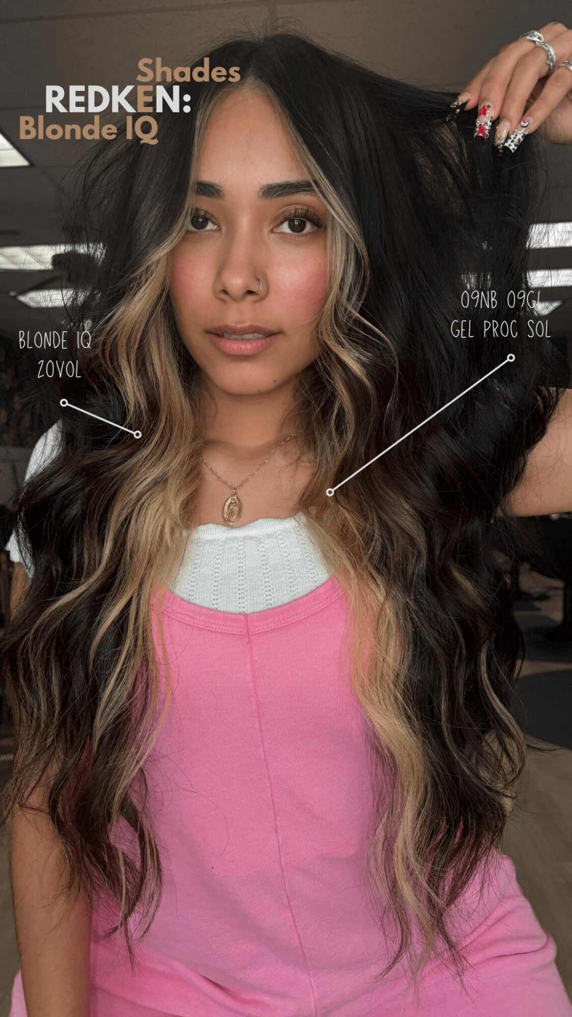Young woman with long wavy hair, wearing a pink and white top, looking at camera, indoors.