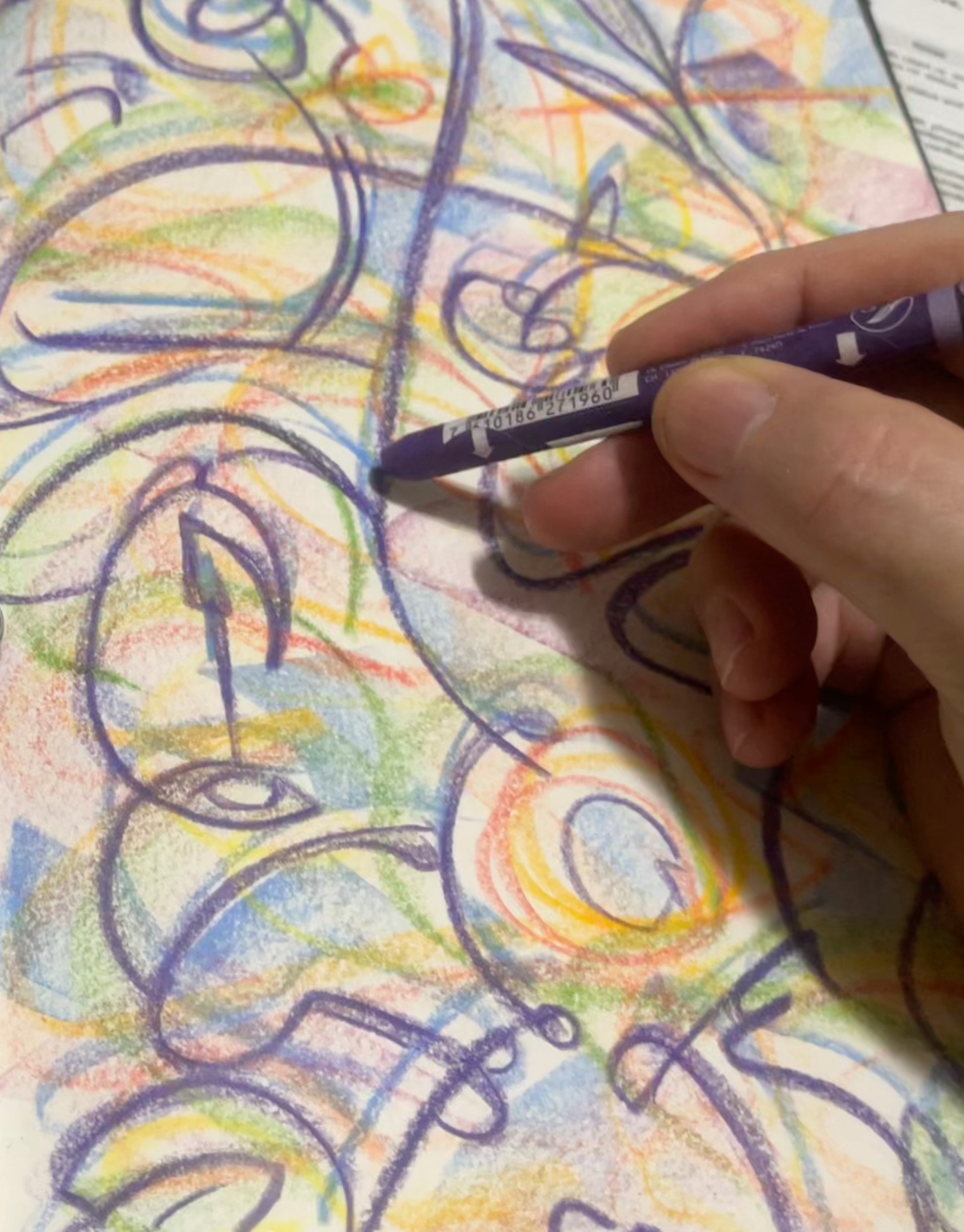 Hand holding a black marker drawing colorful abstract lines on paper, with various overlapping shapes and colors.