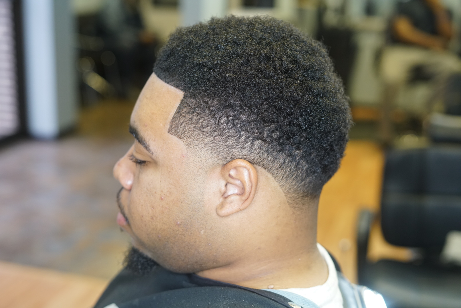 Side view of a young man with a fresh, short haircut in a barbershop, seated in a barber chair.