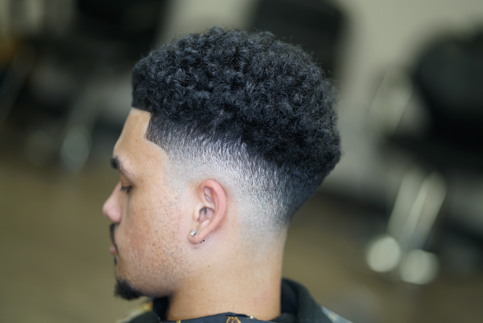 Side profile of a young man with a curly high-top fade hairstyle, blurred background