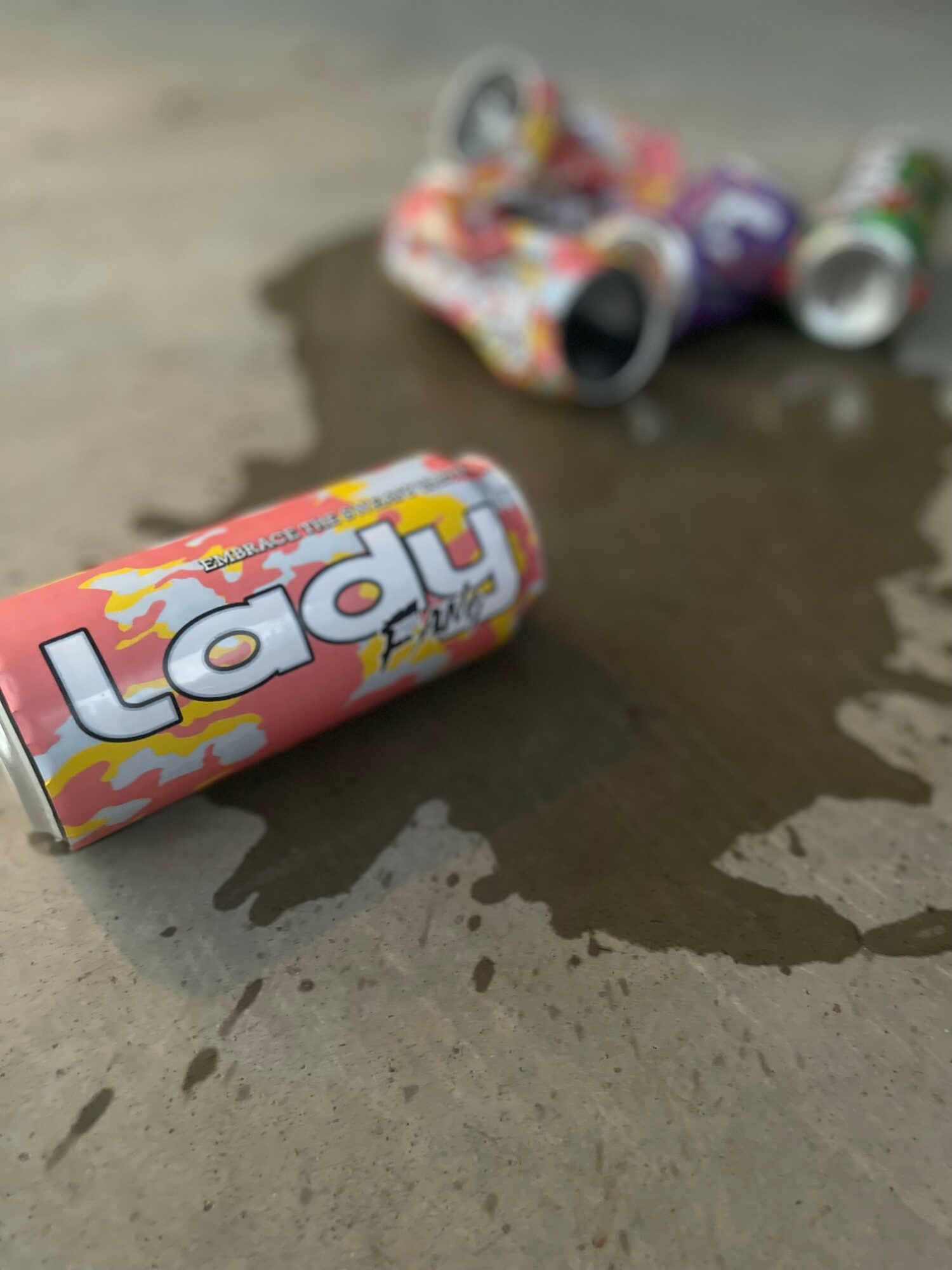 A can of Lady soda on a surface with other cans in the background, some spilled liquid nearby.