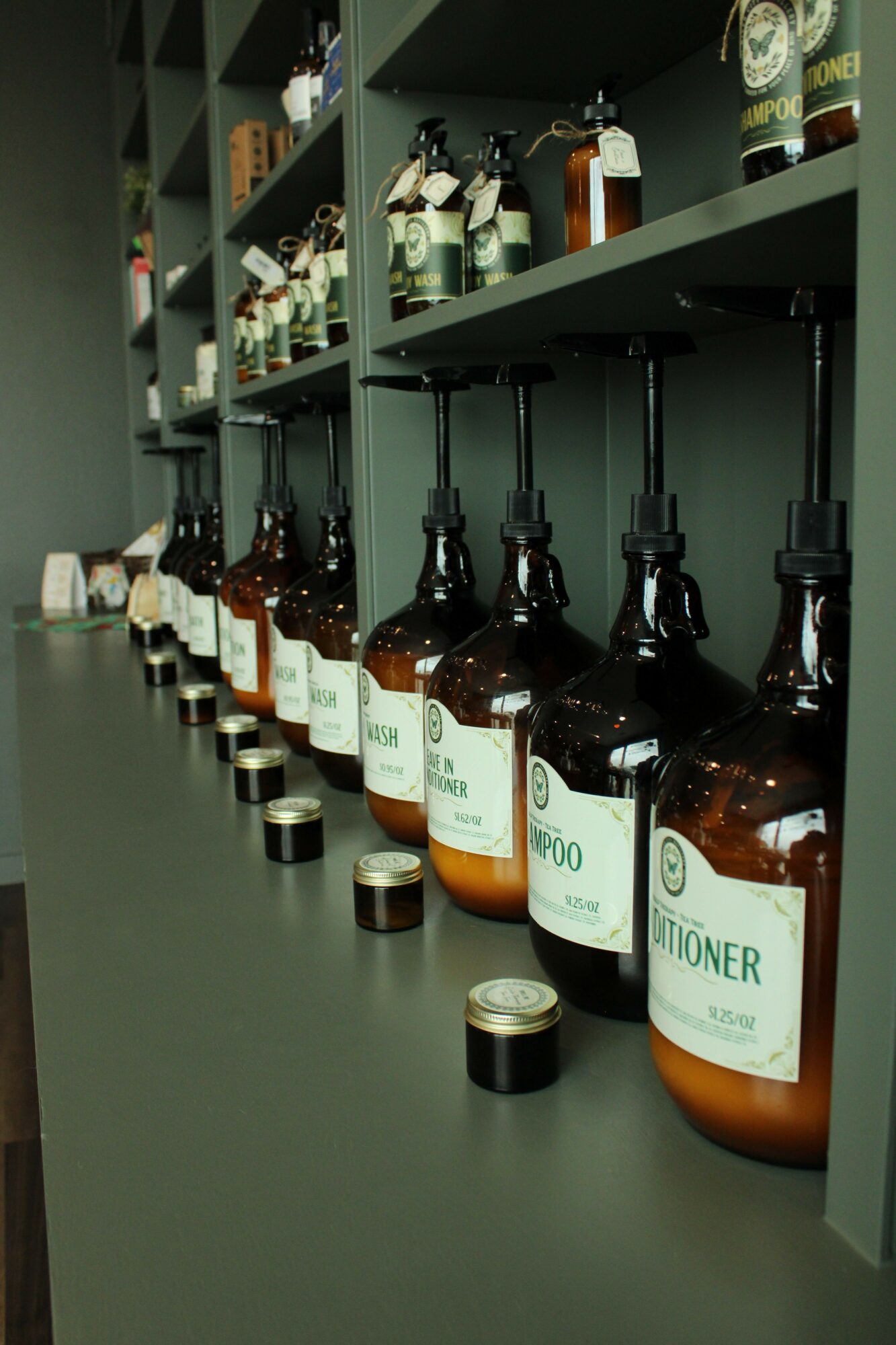 Row of brown bottles with white labels on a table, with shelves containing various items in the background.
