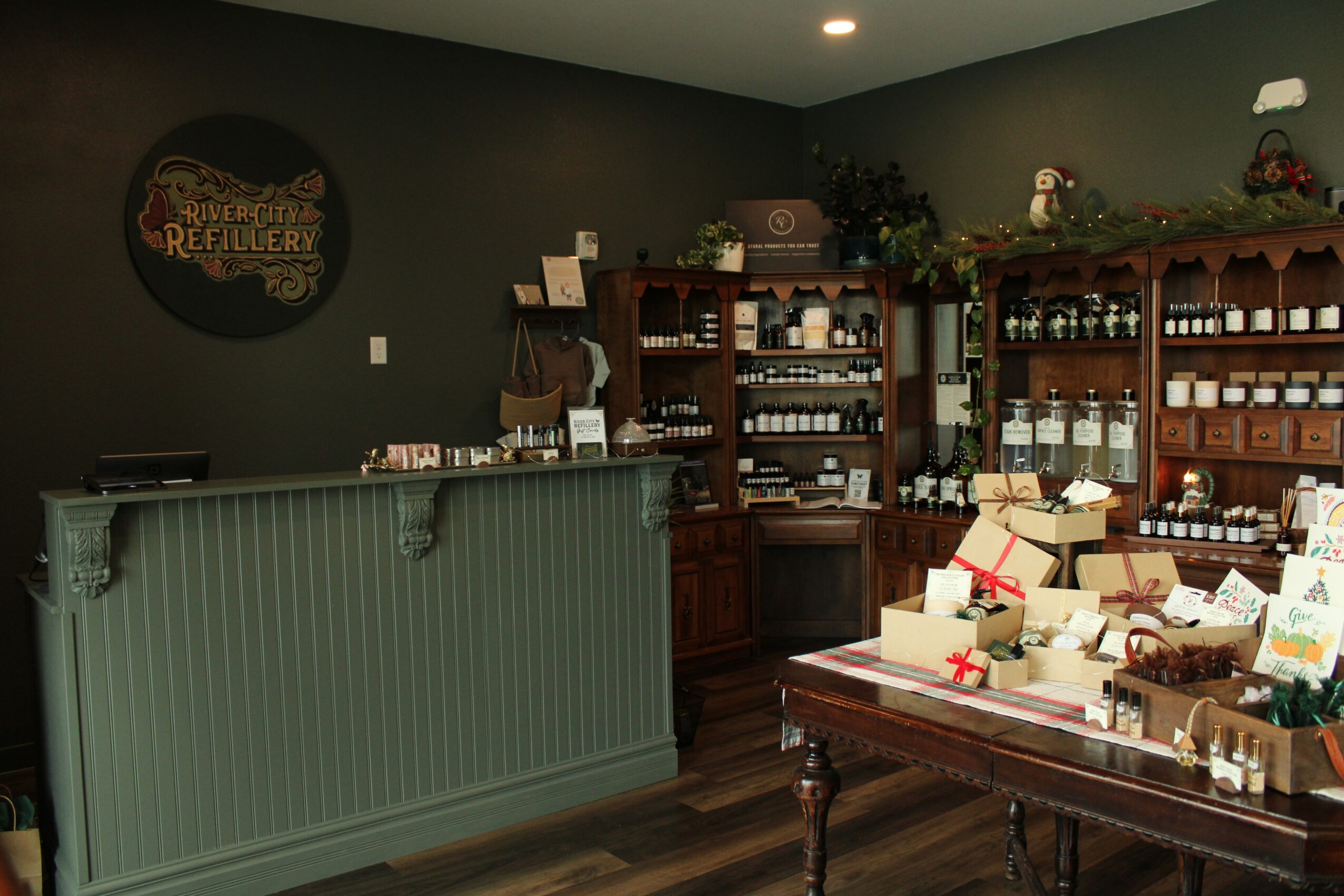 Interior of a shop with a green counter, wooden shelves filled with jars and boxes, and a dark wall with a sign.