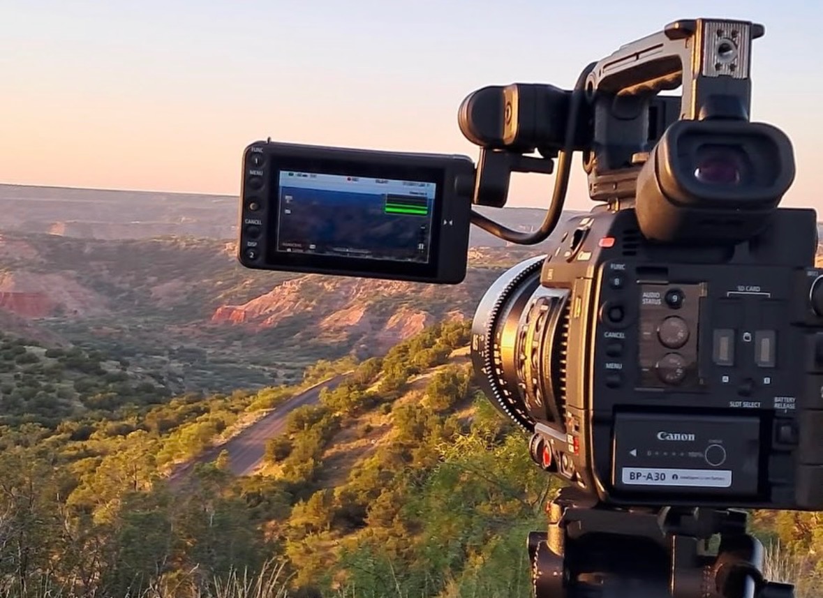 Camera set up on tripod overlooking a landscape with hills and trees during sunset.