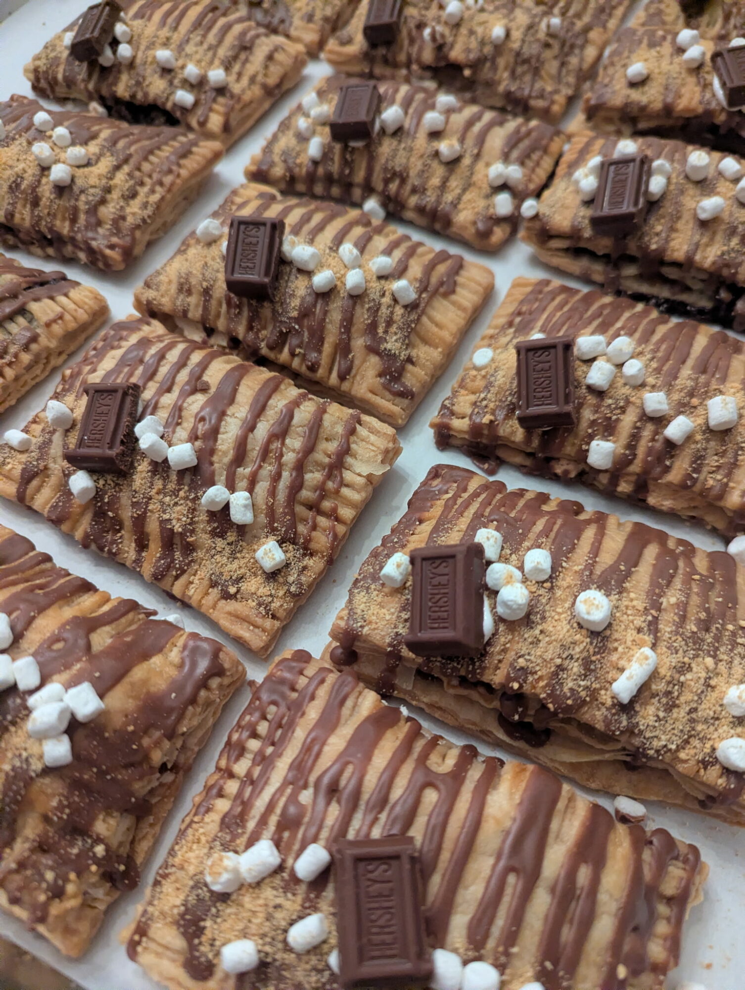 Multiple rectangular chocolate-covered bars decorated with chocolate drizzle, small white candies, and chocolate pieces on a white surface.