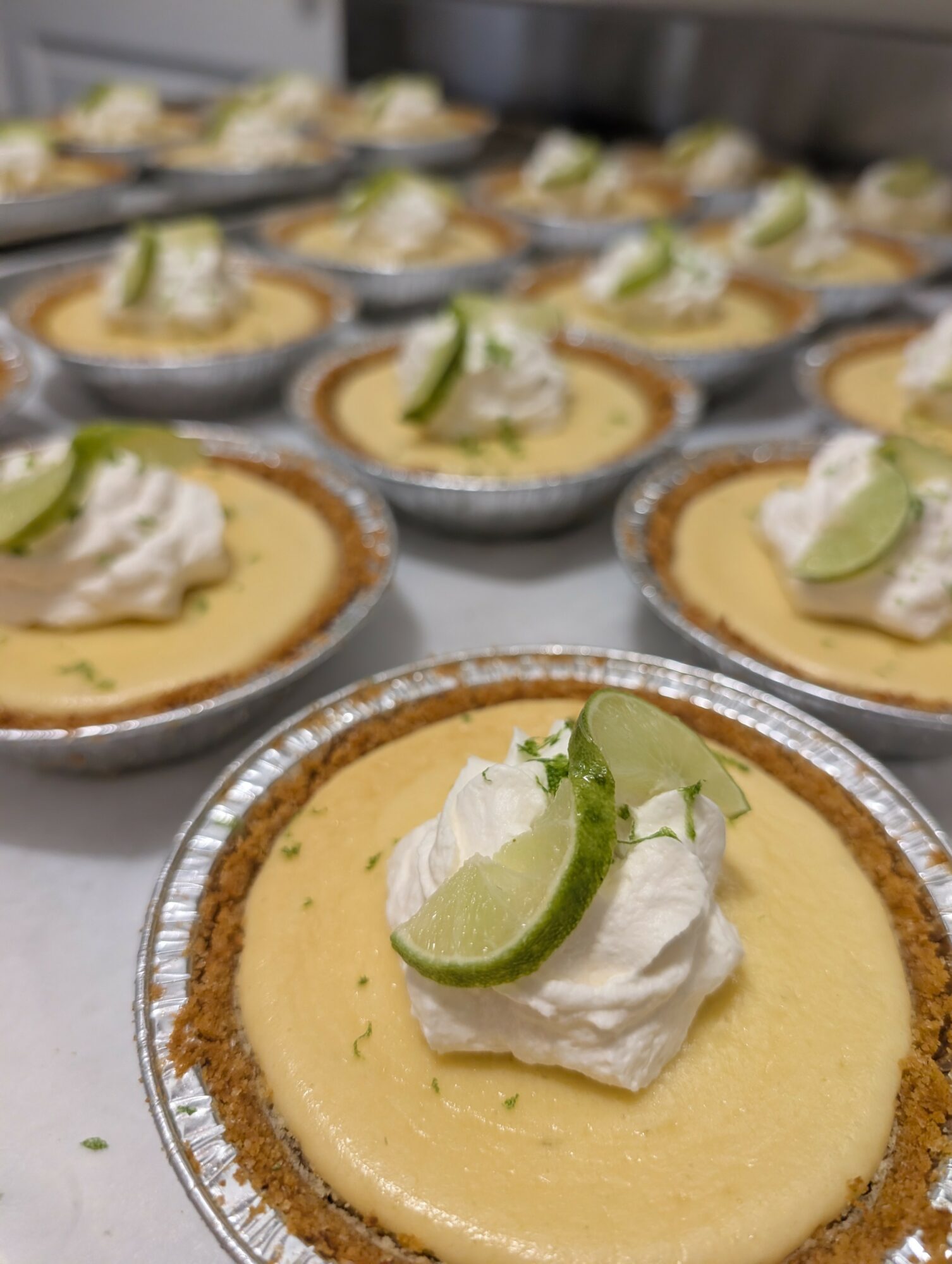 Lemon tart with whipped cream and lime slice on top, arranged on a tray, close-up view.
