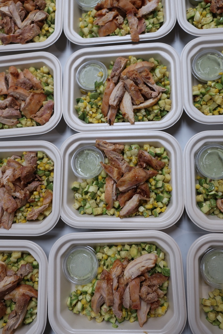 Multiple meal containers filled with rice, grilled meat, and a small container of sauce, arranged in a grid pattern.
