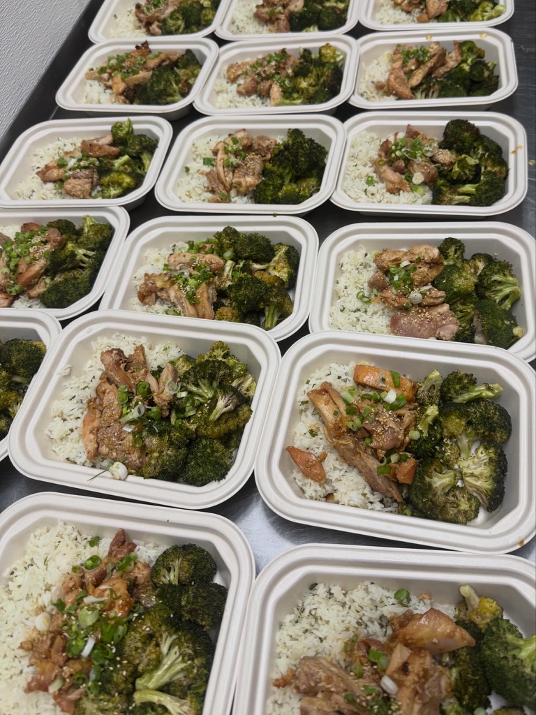 Multiple meal containers with rice, broccoli, and meat dishes arranged in rows.
