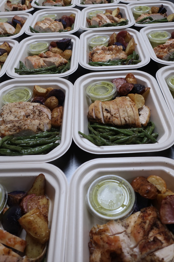 Multiple meal containers with chicken, green beans, potatoes, and sauce, arranged in rows on a surface.