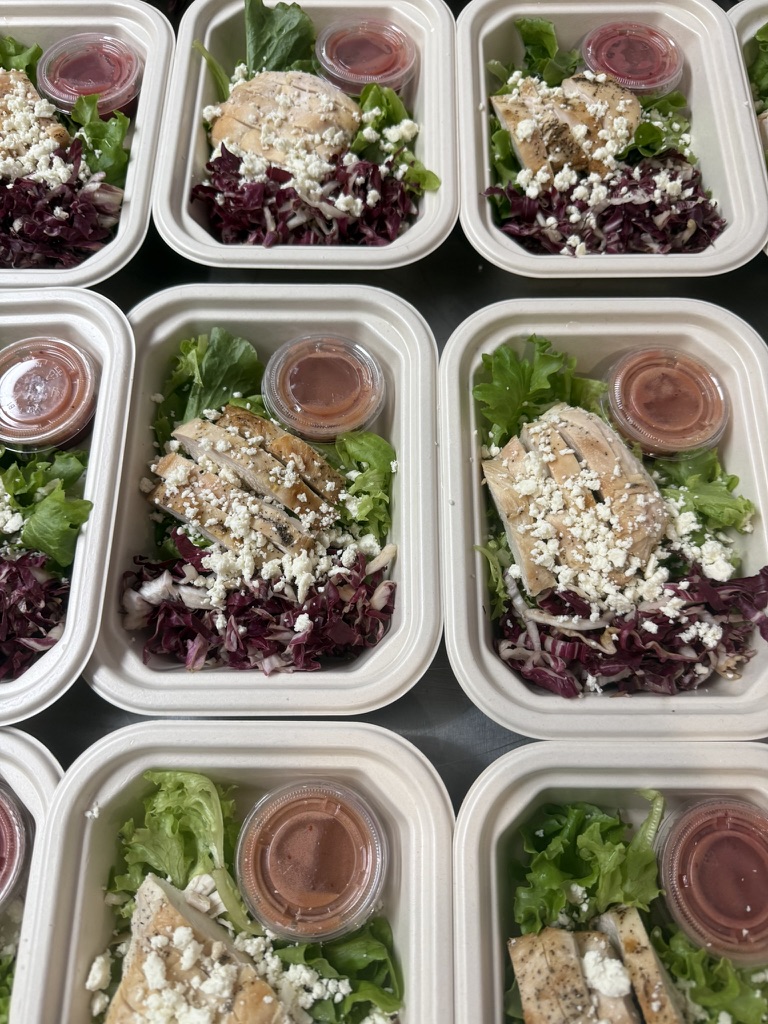 Pre-packaged salads with lettuce, shredded cheese, dressing, and a slice of bread in containers.