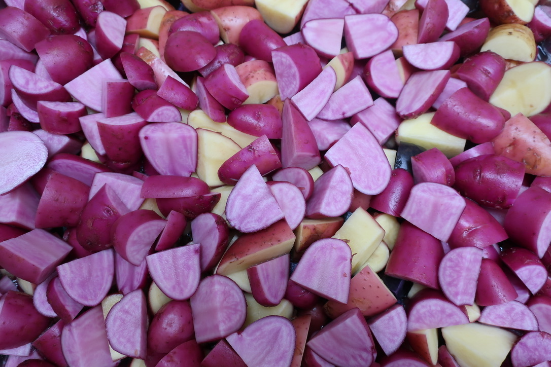 Close-up of chopped red, purple, and yellow vegetables, possibly radishes or onions, with varied shapes and sizes.