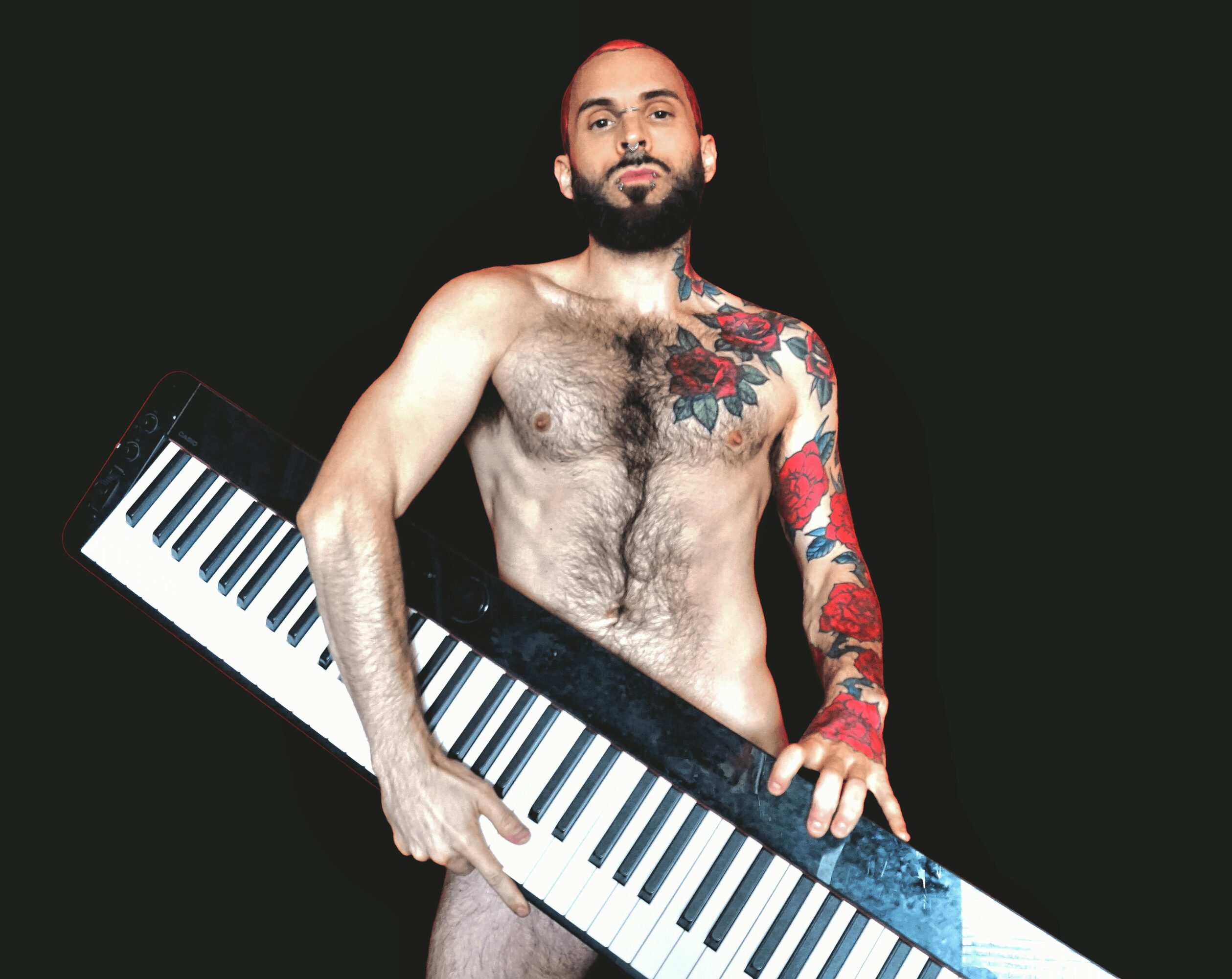 Naked man with tattoos holding a keyboard against a black background.