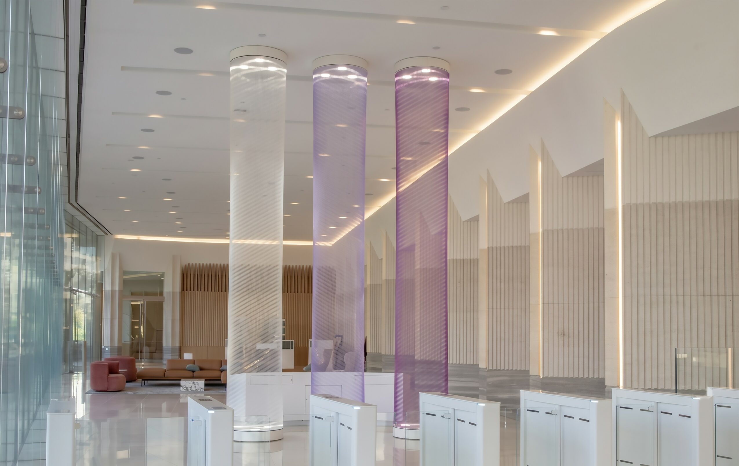 Interior space with tall, illuminated cylindrical columns in white, purple, and pink, and modern design elements.