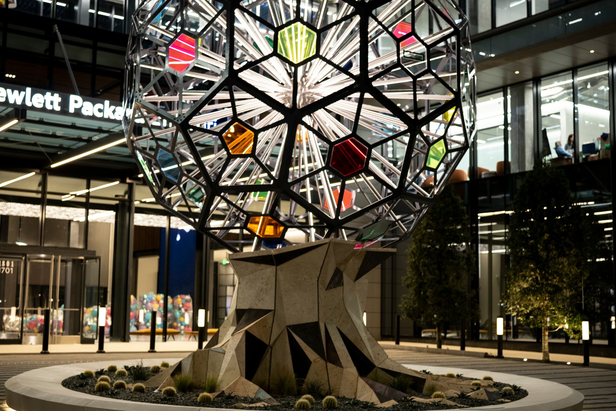 Colorful geometric sculpture of a heart atop a stylized tree trunk in a modern shopping mall.