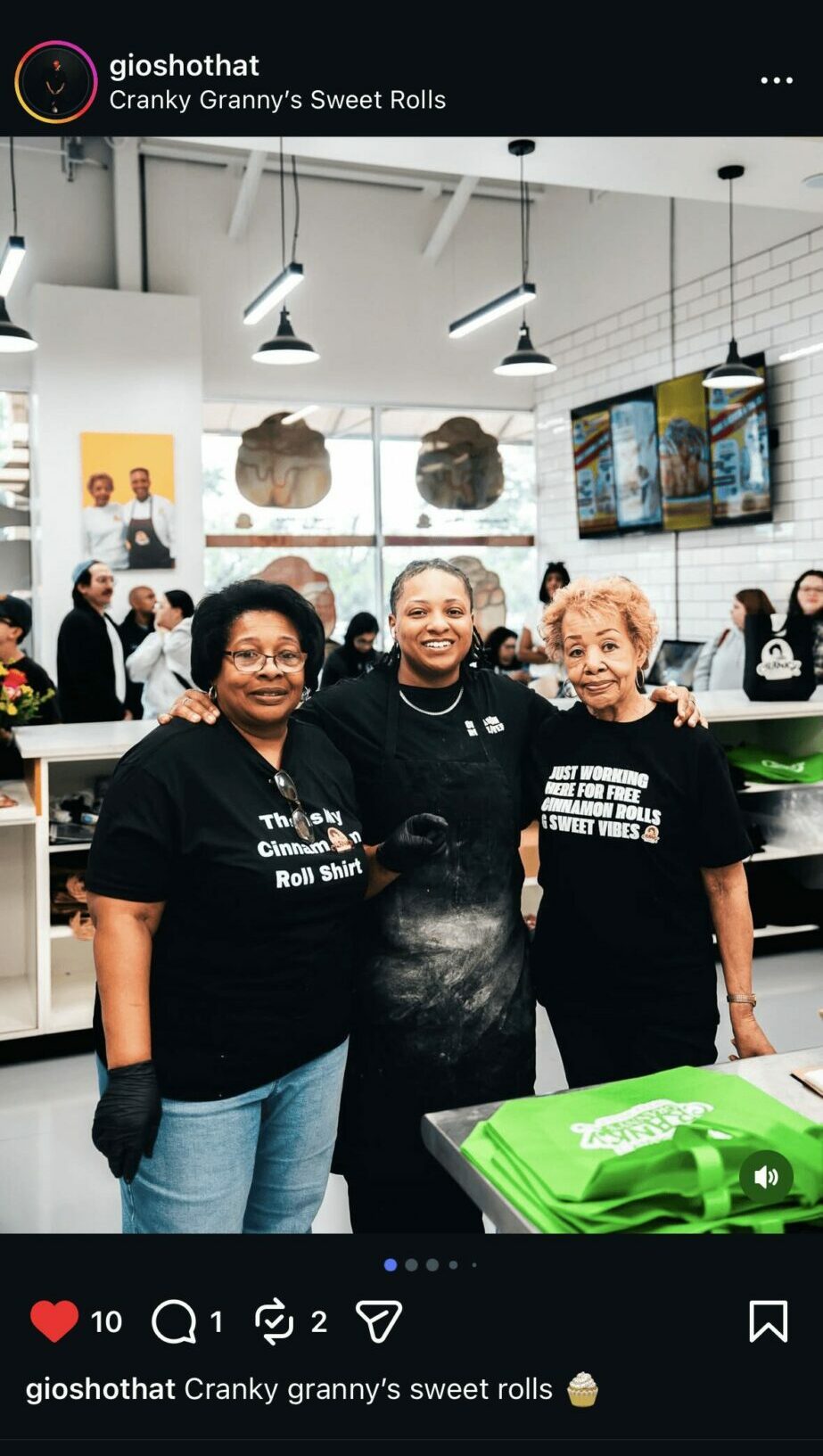 Three women standing together in a restaurant, smiling, with a dog in front of them, and people in the background.