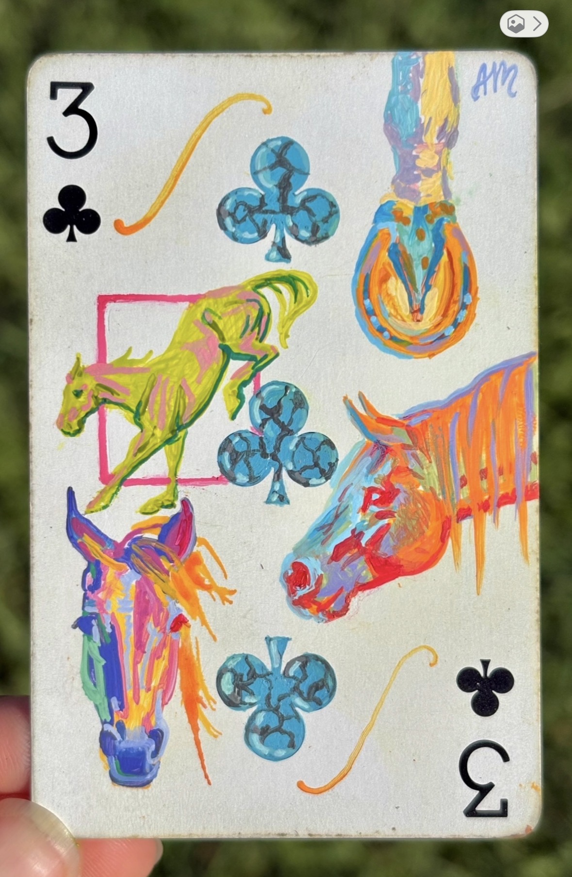Playing card with colorful horse, horse head, club symbols, and a number three, upside down.