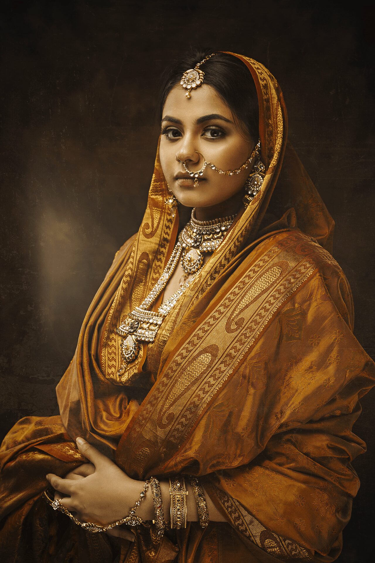 Woman in traditional Indian attire with jewelry, wearing a brown and gold saree, looking to the side.