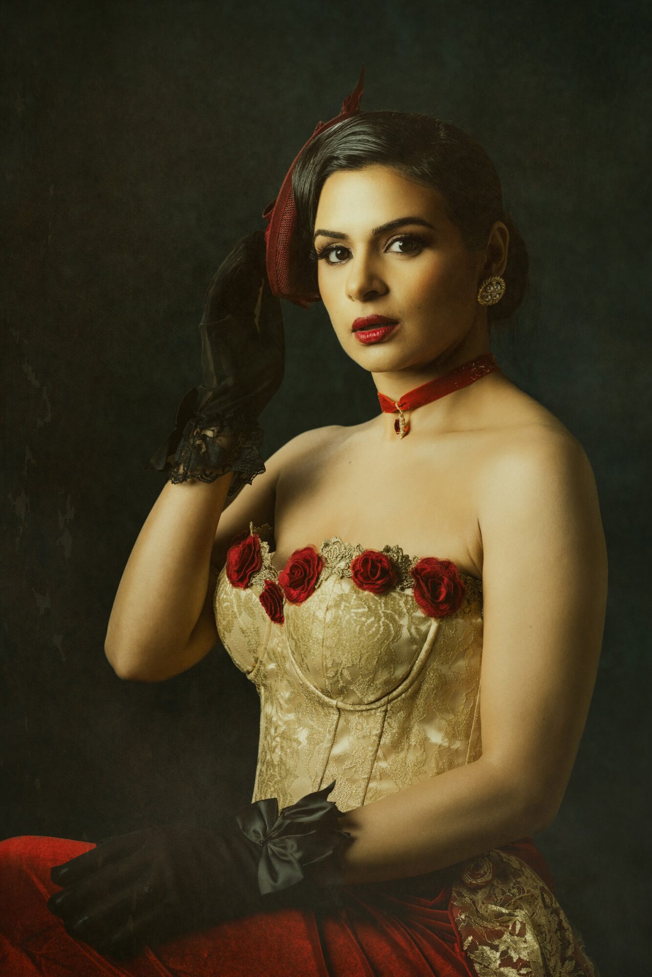 Woman in vintage dress with red roses, black gloves, and jewelry, posing against dark background.