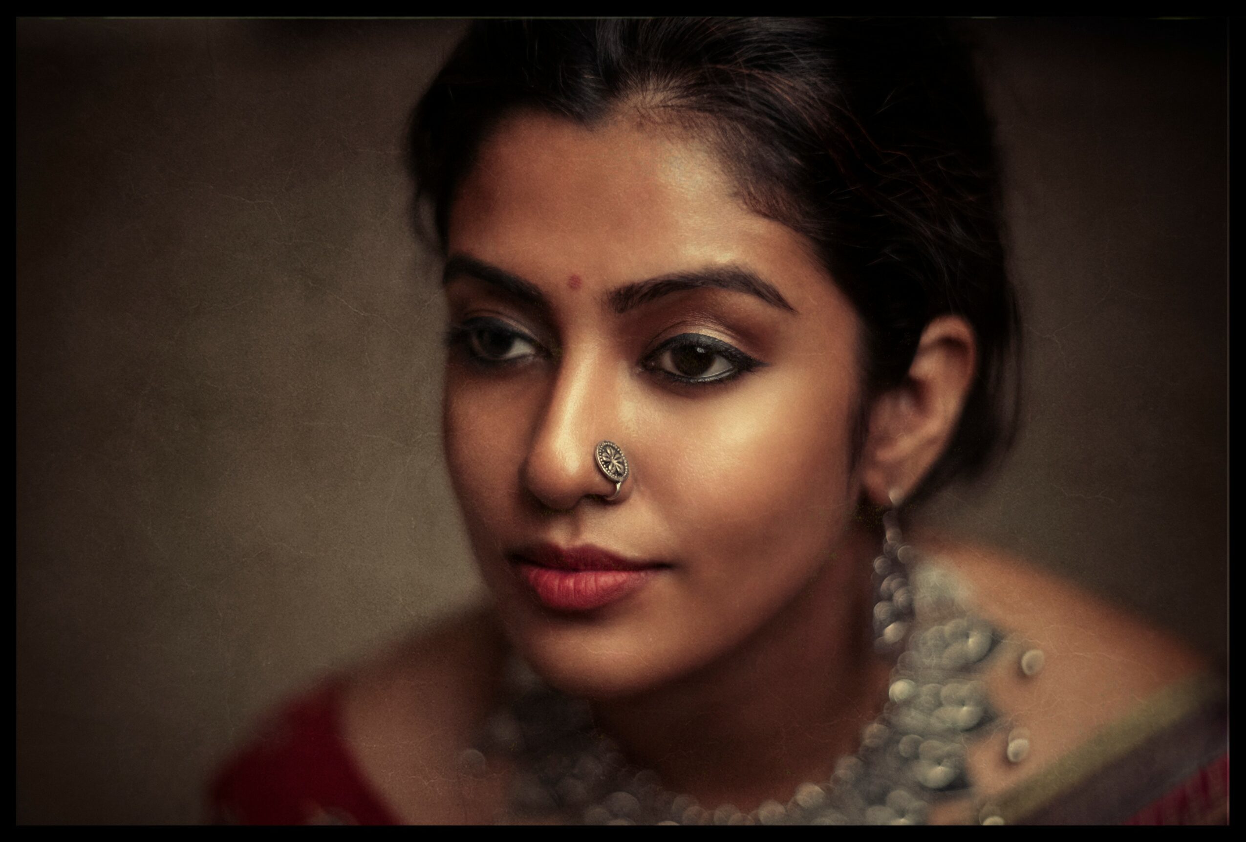 Portrait of a woman with traditional jewelry and makeup, looking slightly downward, with a neutral background.