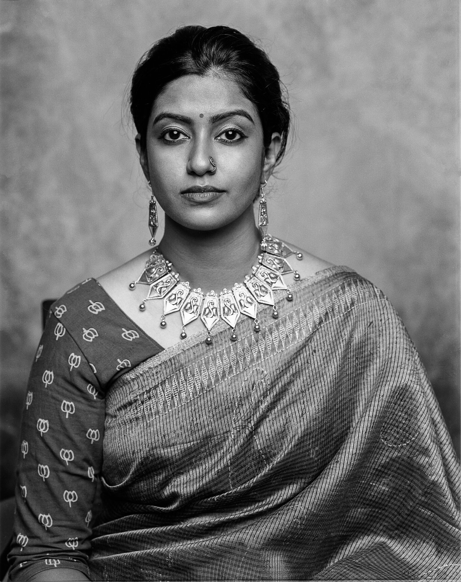 Portrait of a woman wearing traditional attire and jewelry, looking directly at the camera, with a neutral background.
