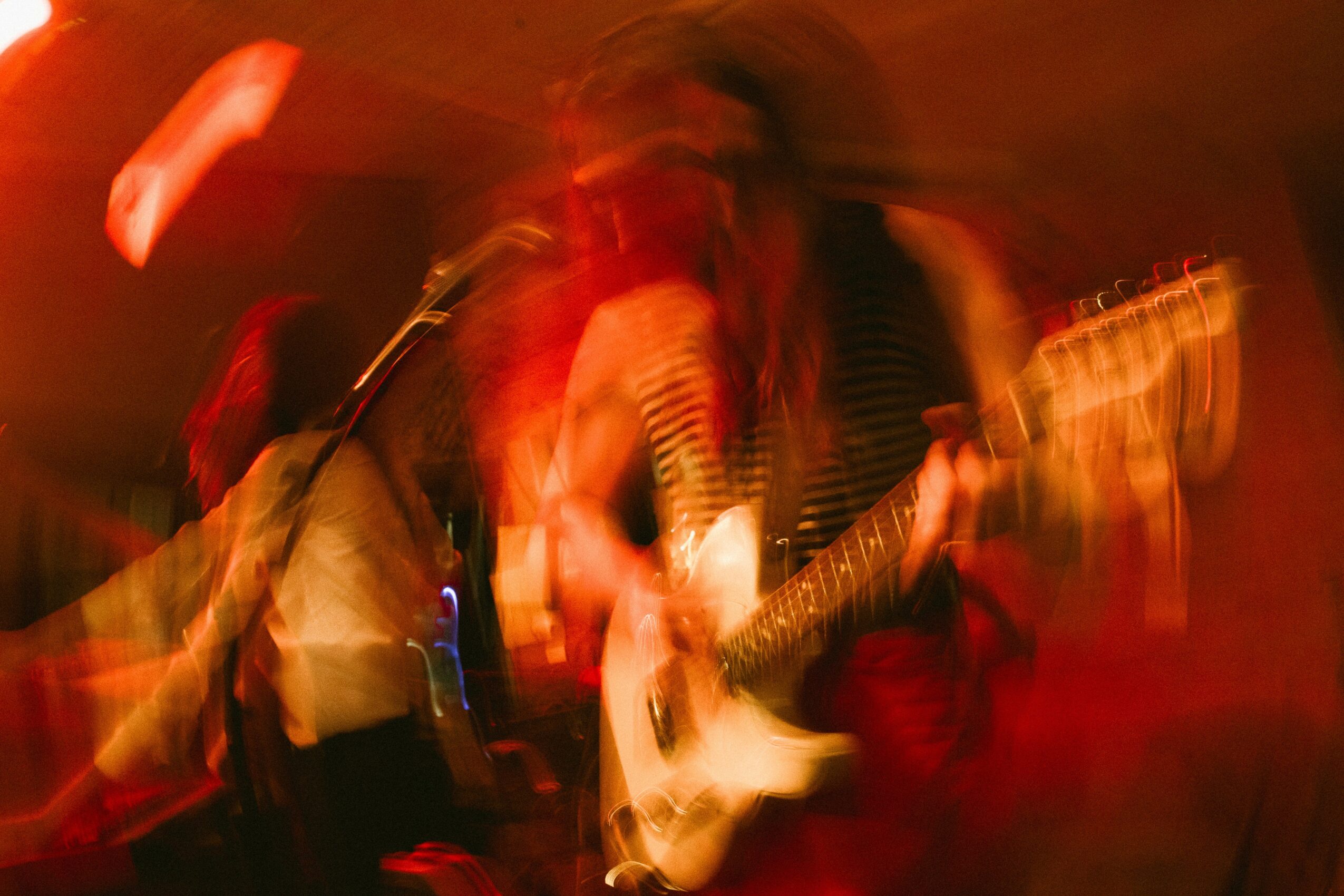 Blurred image of a person playing an electric guitar in a dimly lit setting.