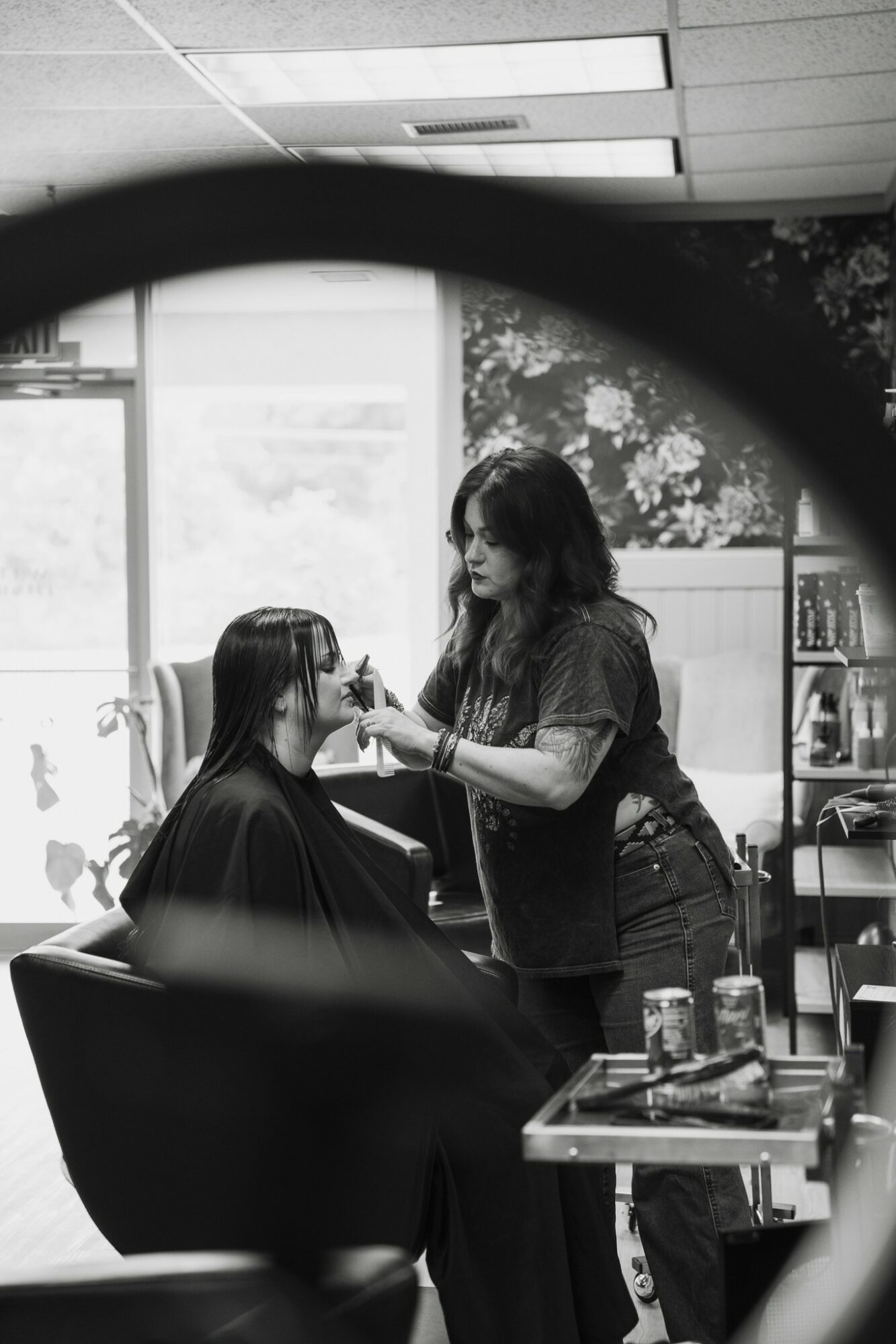 A person getting their hair styled by a hairstylist in a salon, with a window and shelves in the background.