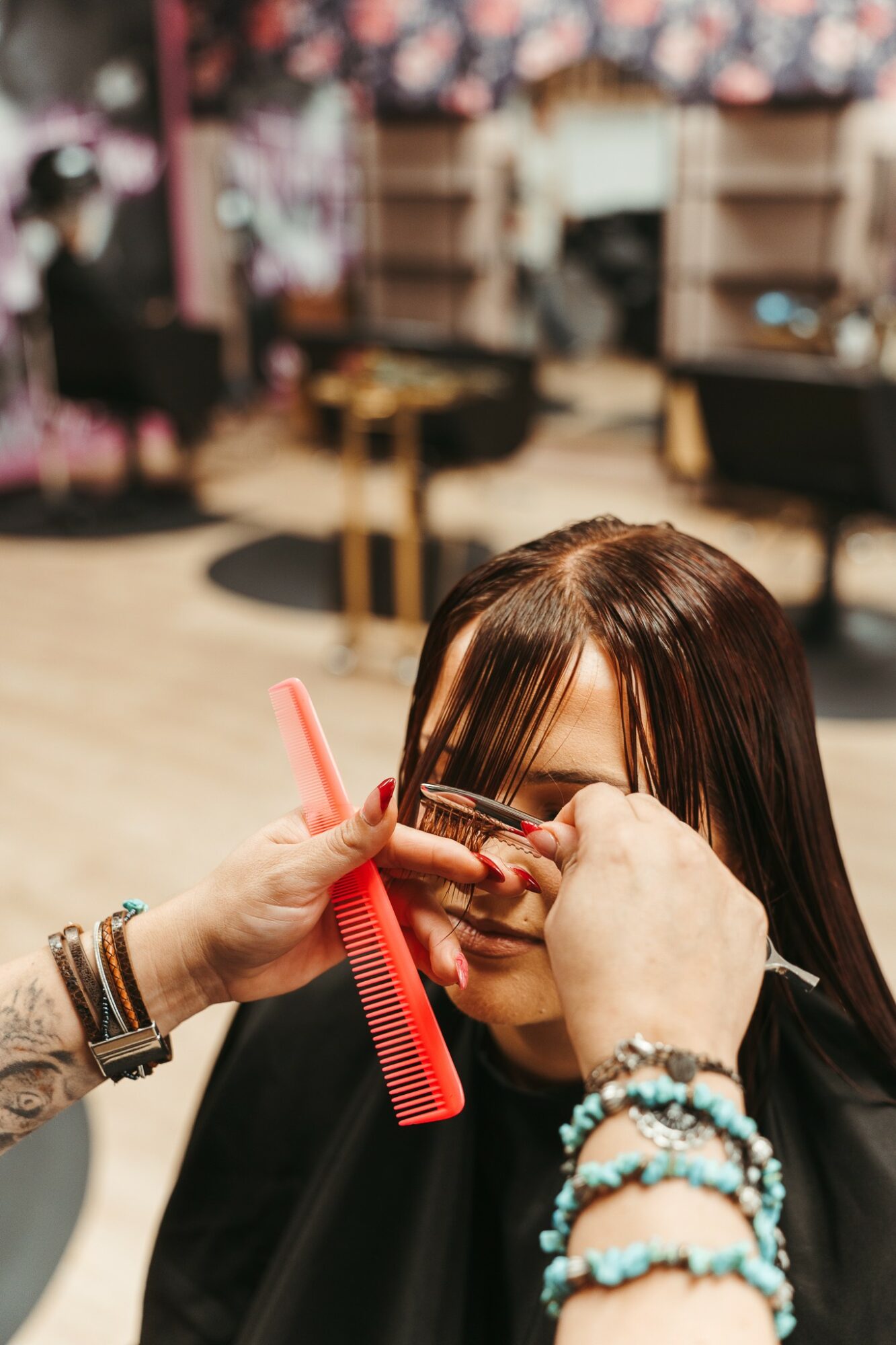 A person getting their eyebrows shaped with a comb and brush, surrounded by jewelry, in a salon setting.