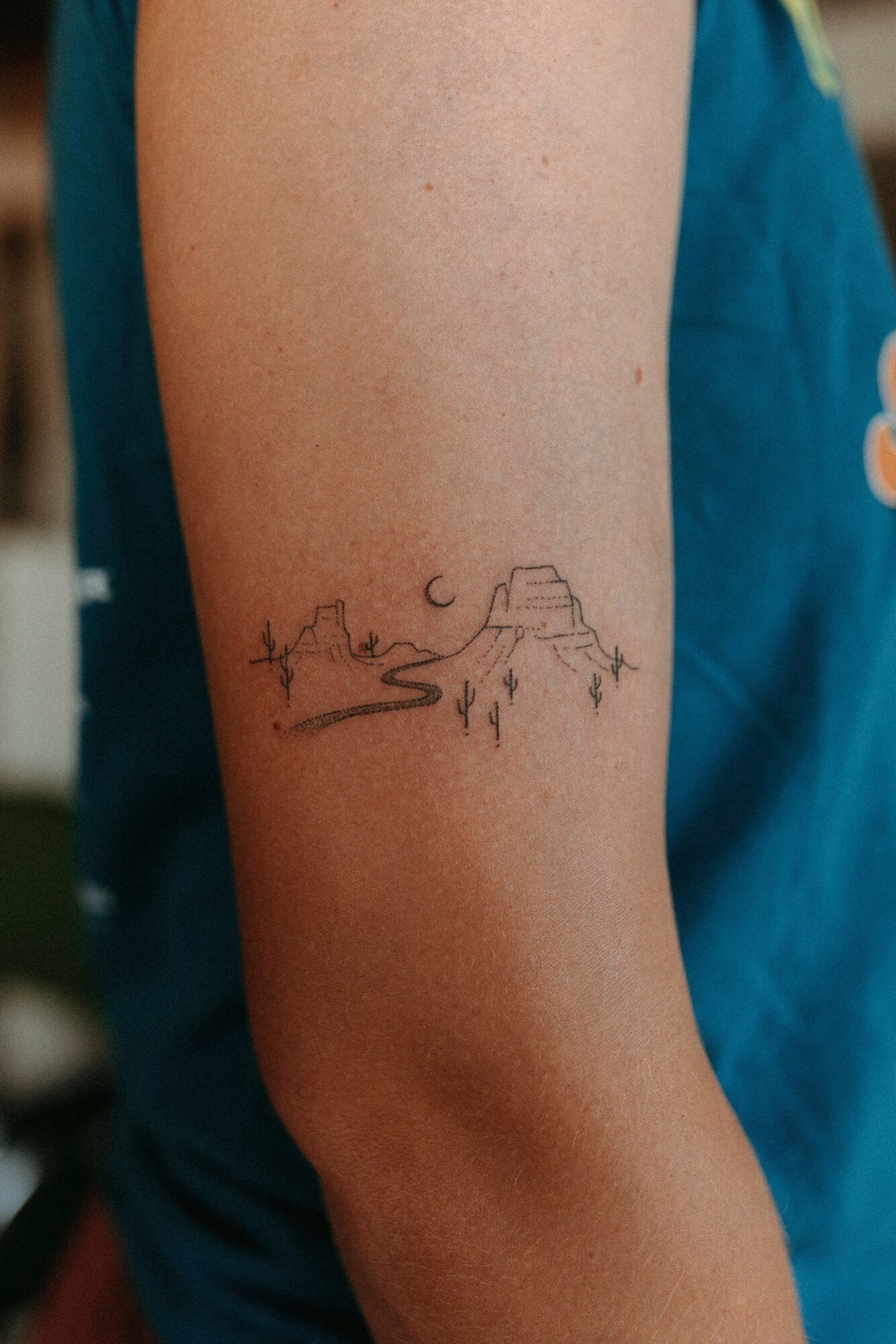 Tattoo of a mountain, river, and trees on person's upper arm, with a star and moon in the sky.