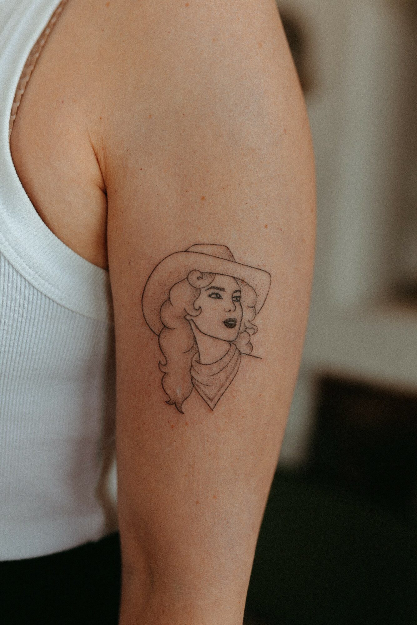 Line drawing of a woman with wavy hair wearing a wide-brimmed hat on upper arm.