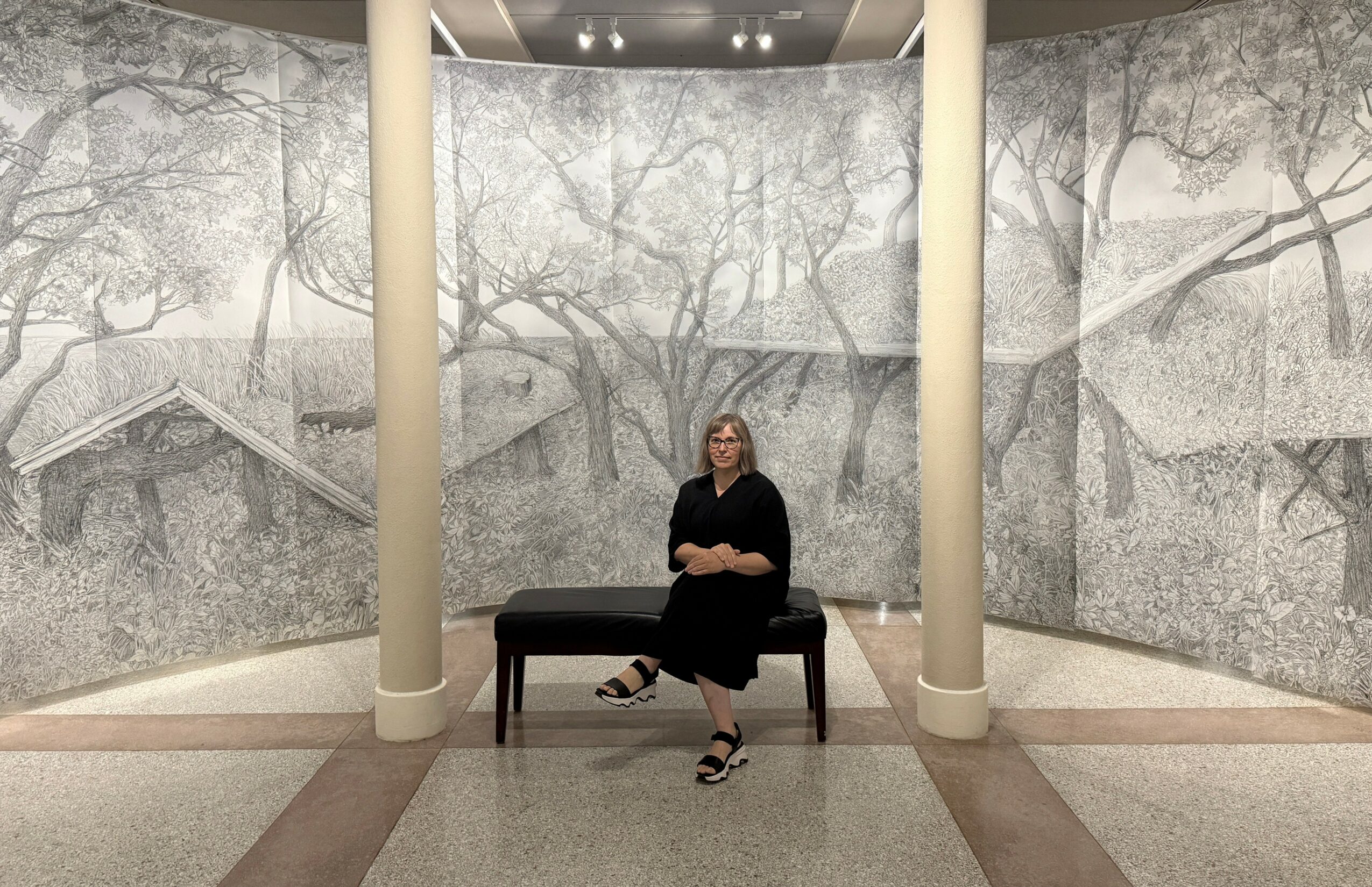 Woman sitting on a bench in a circular room with mural walls and two large columns.