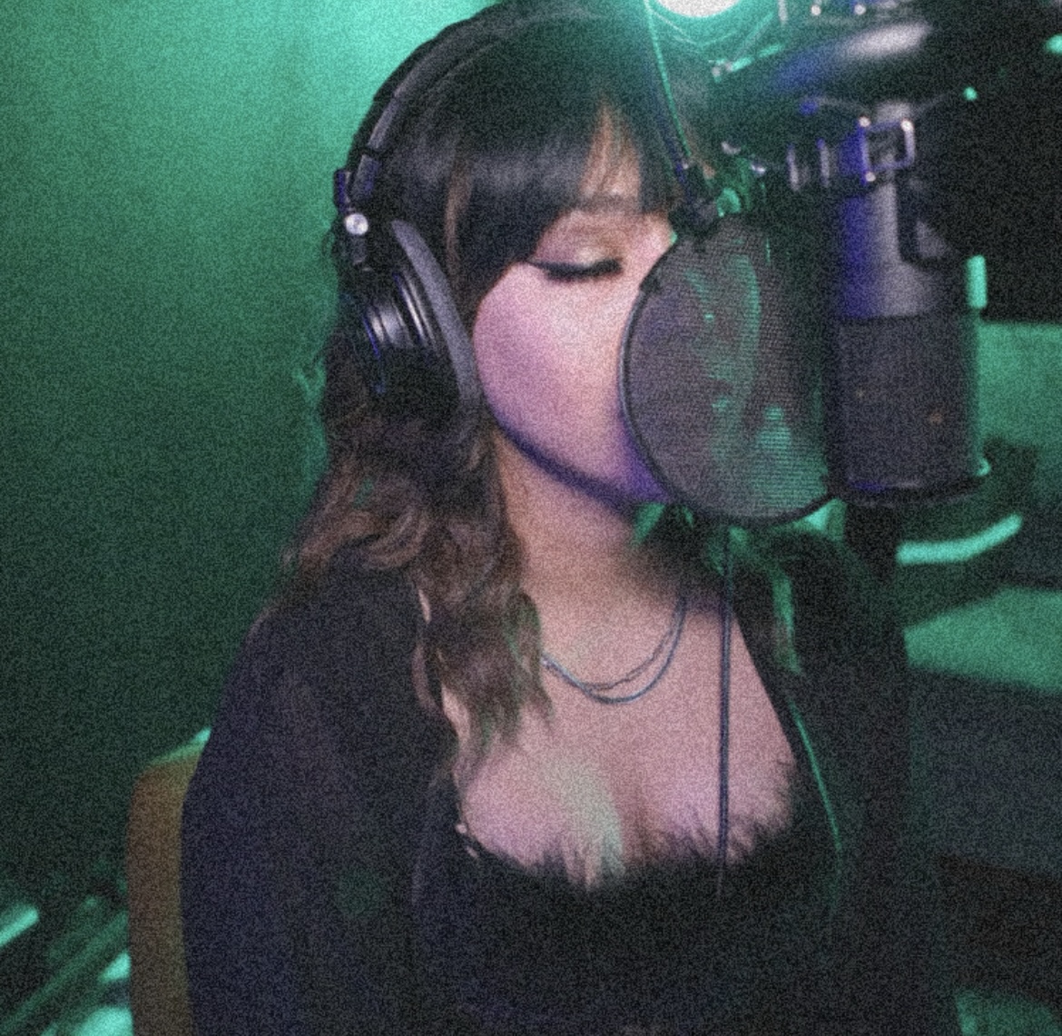 Woman with long hair and headphones singing into a microphone in a recording studio.