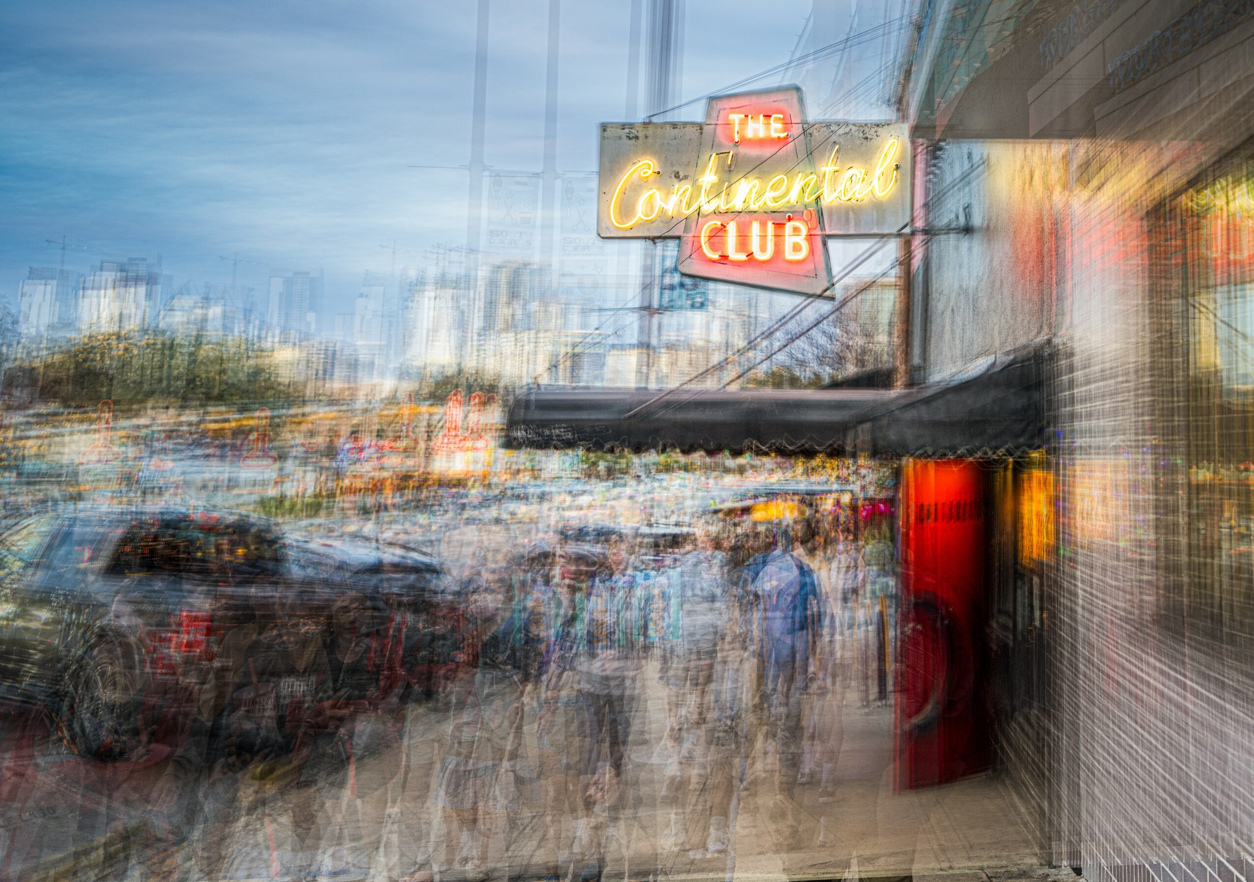 Blurred view of a street scene with a neon sign reading 'Continental Club' and people walking outside.