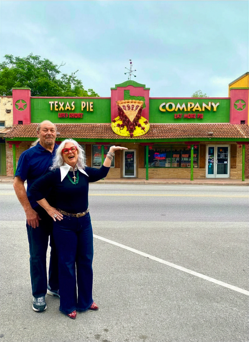 Two people standing in front of a colorful restaurant with a sign reading 'Texas Pie Company.' The building has pink, green, and yellow colors.