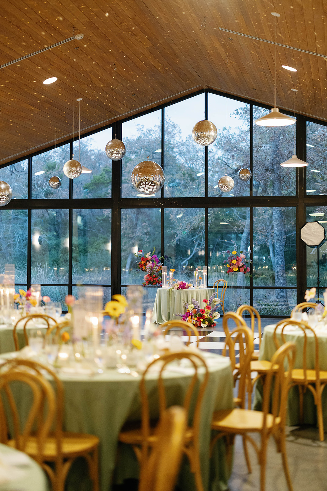 Elegant dining area with round tables, chairs, floral centerpieces, and large windows with hanging pendant lights.