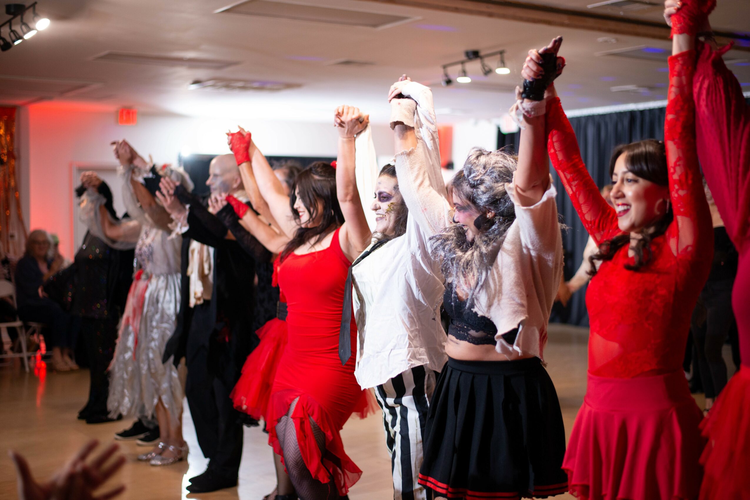 Group of people dancing with arms raised, some in costumes, in a decorated indoor space, celebrating joy.