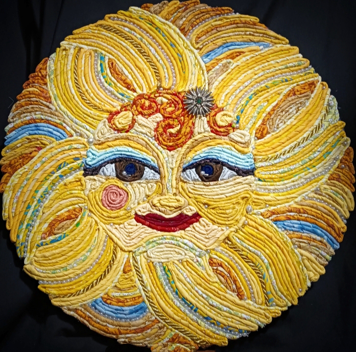 Colorful sun face made of piped frosting with detailed eyes, nose, and smiling mouth, surrounded by yellow and orange rays.