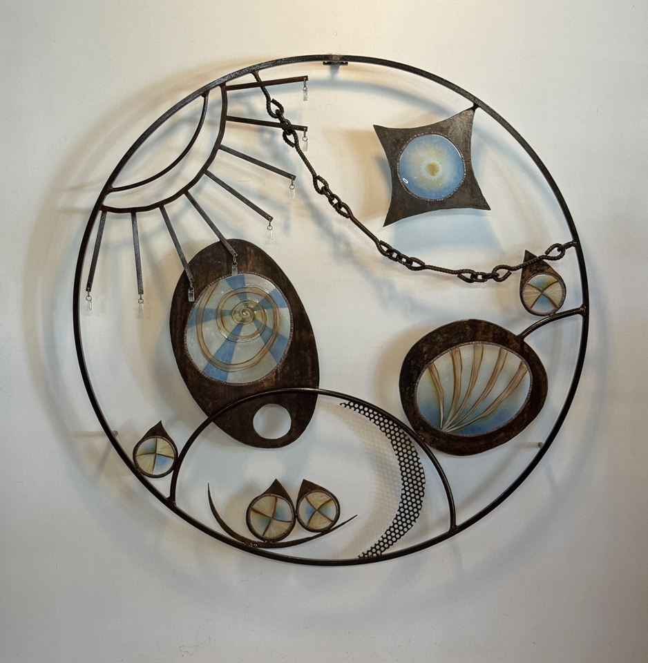 Decorative wall clock with abstract geometric shapes and metal frame, no visible numbers or hands, mounted on a white wall.