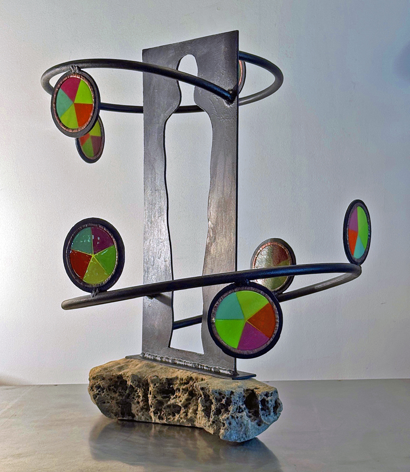 Metal sculpture with circular colored segments on rods, mounted on a stone base, against a plain background.