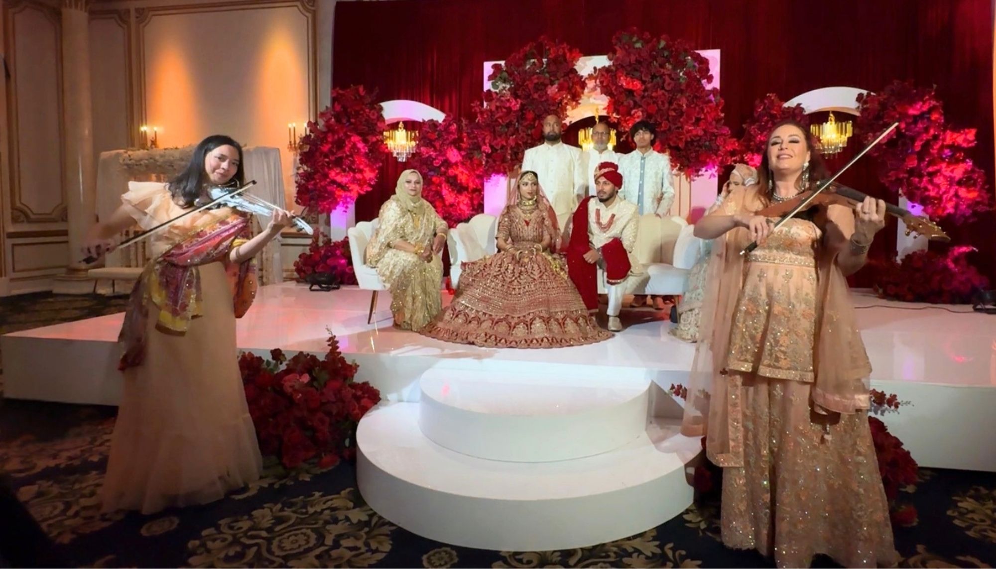 People in traditional attire on a decorated stage with floral arrangements and a central platform, performing music and dance.