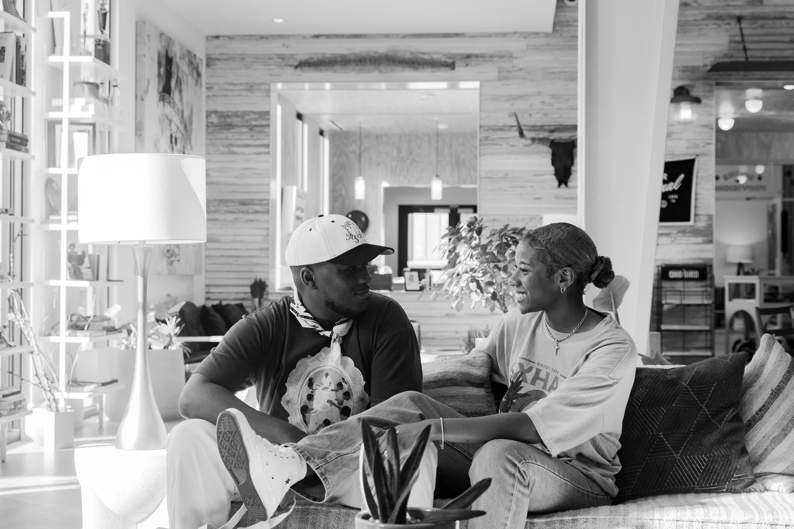 Two people sitting on a couch, engaged in conversation, in a cozy indoor setting with a lamp and decorative elements.