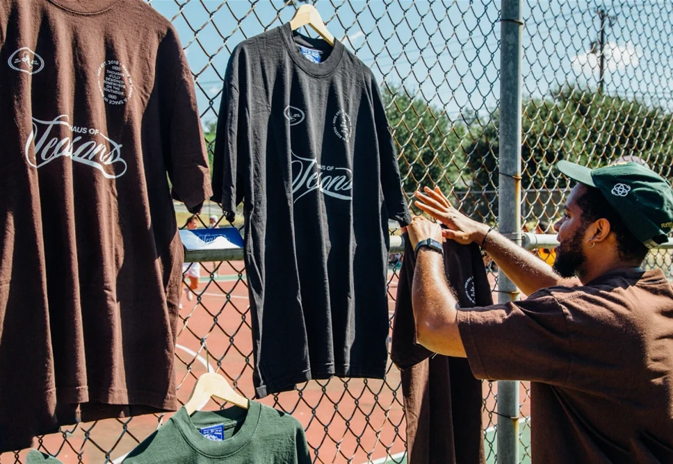 Person hanging black sports jersey on chain-link fence, with other jerseys displayed nearby, outdoors on sunny day.